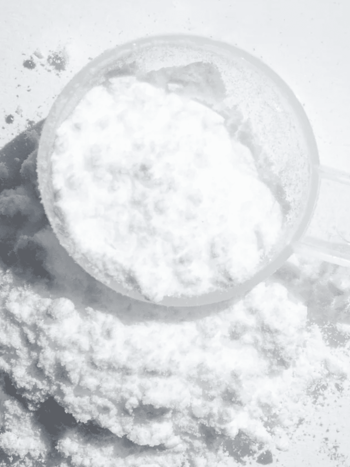 A clear plastic scoop filled with white powder rests on a small pile of the same powder, against a white background.