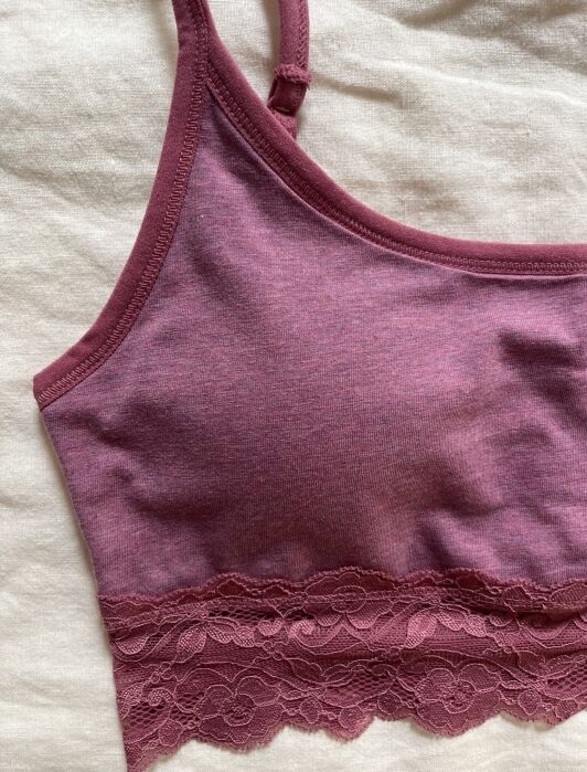 Mauve bralette with adjustable straps and lace trim detail along the band, laid flat on a light fabric background.