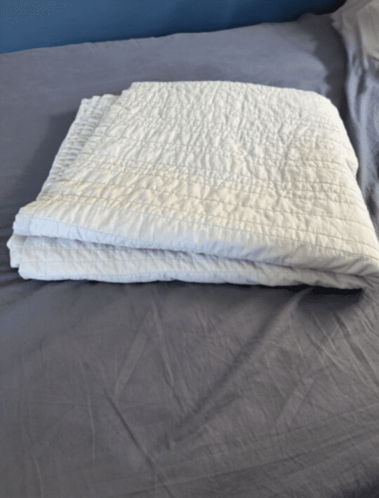A neatly folded white quilt lies on a gray bedspread in a tidy bedroom.