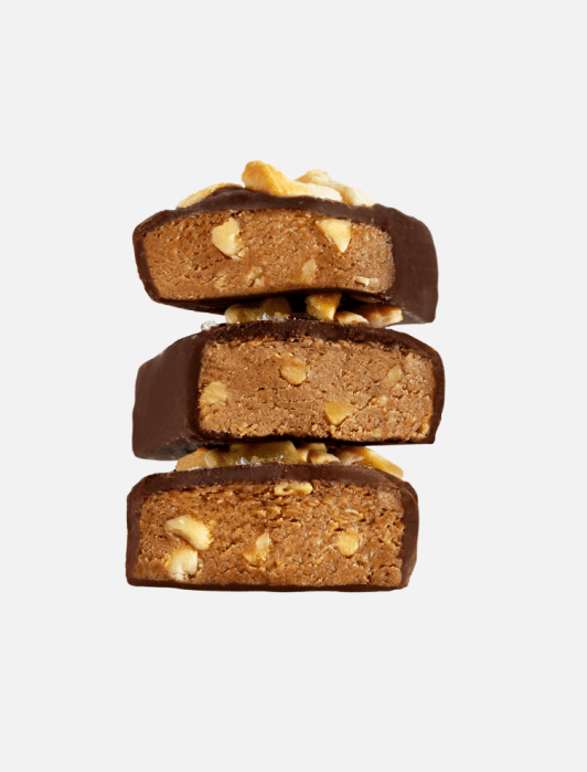Three chocolate-coated protein bars with visible nuts are stacked on top of each other against a plain white background.