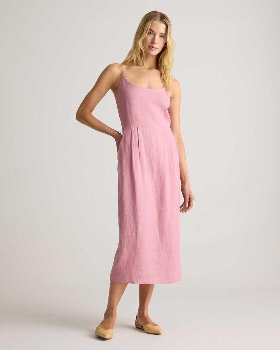 A woman stands in a studio wearing a sleeveless, light pink midi dress with a square neckline and beige flats.