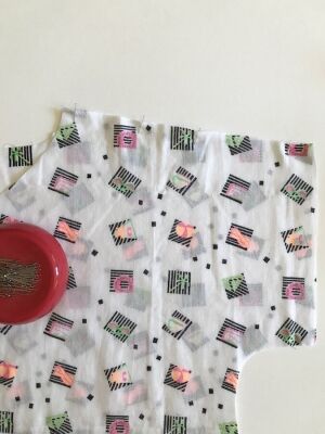 A piece of white patterned fabric with pins in it.
