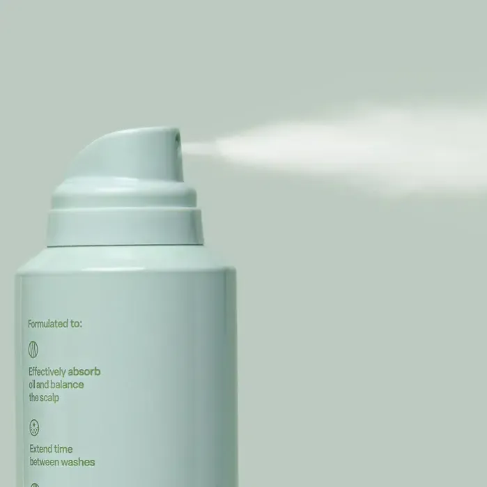 A spray can releasing mist against a light green background, with text on the can detailing its benefits for scalp care.