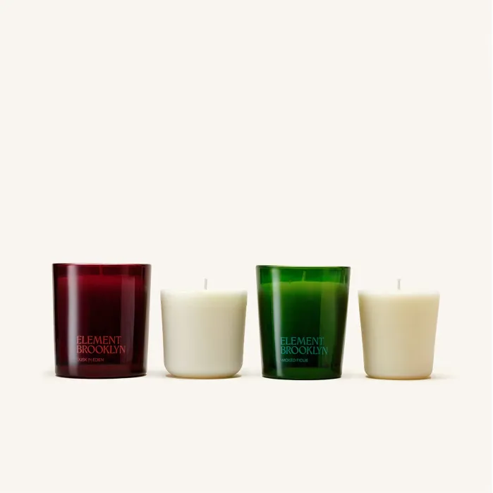 Two white votive candles and two votive candle holders, one red and one green, both labeled “Element Brooklyn,” set against a plain light background.