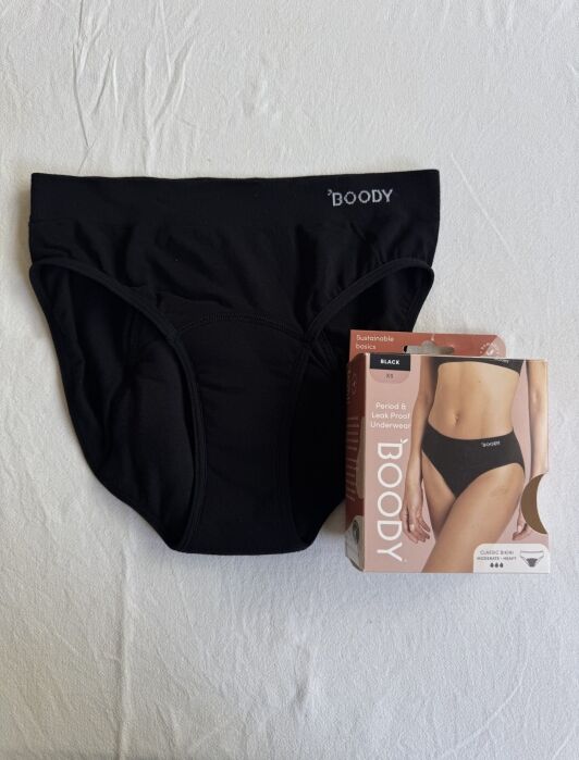 Black period and leak-proof underwear displayed alongside its packaging on a white surface.