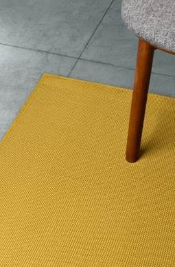 Chair leg on a yellow rug next to a gray tiled floor.