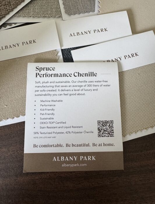 A card describes "Spruce Performance Chenille" fabric by Albany Park, listing features like machine washable, pet-friendly, and sustainable, with fabric swatches and business cards nearby.