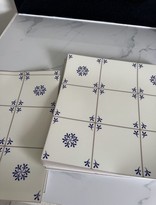 Two stacks of white ceramic tiles with blue floral and corner designs are placed on a white marble surface.