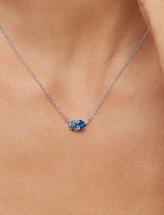 A close-up of a woman's neck wearing a delicate silver chain necklace with a small blue gemstone pendant.