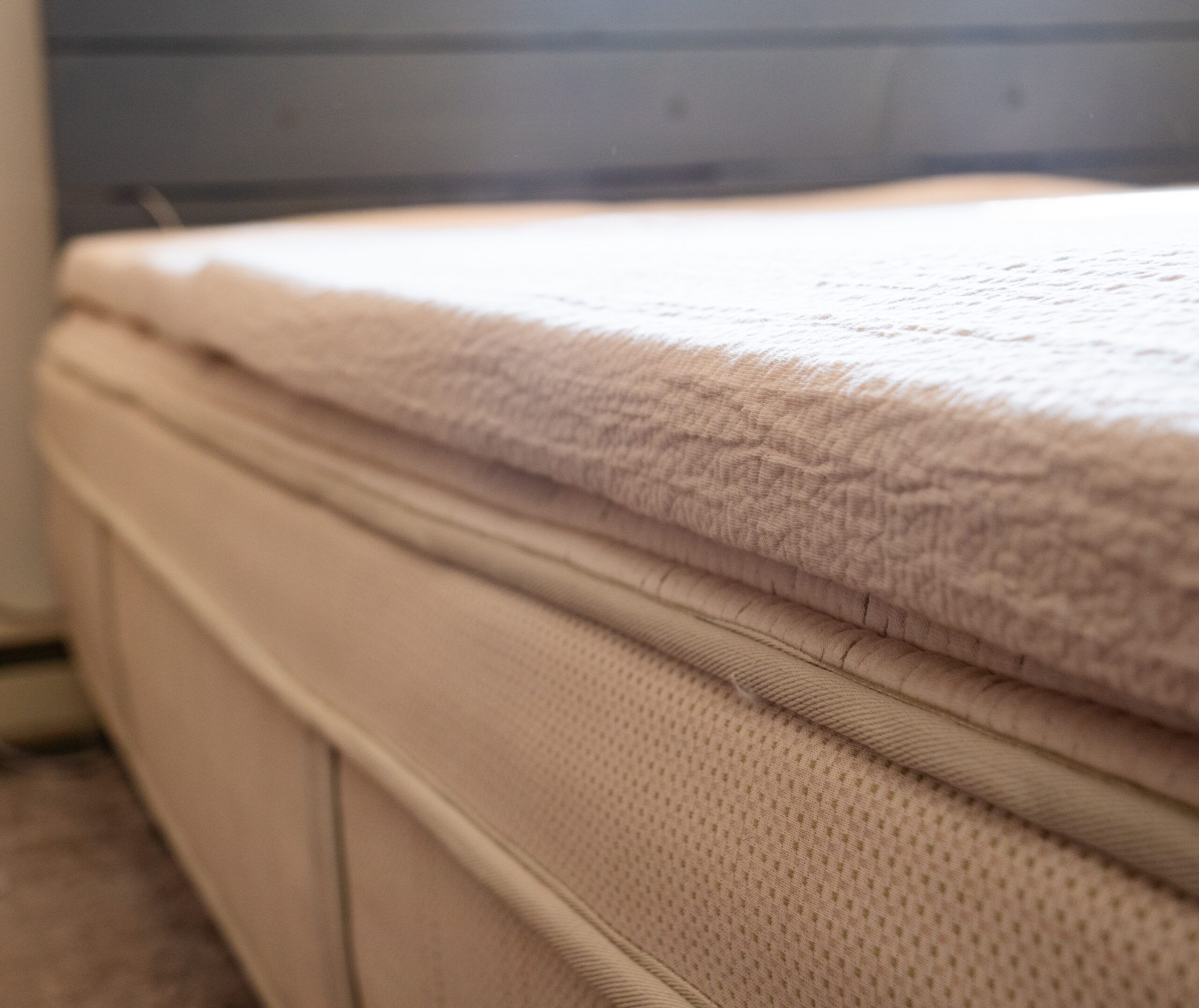 Close-up view of a beige mattress with a textured mattress topper in a softly lit room.
