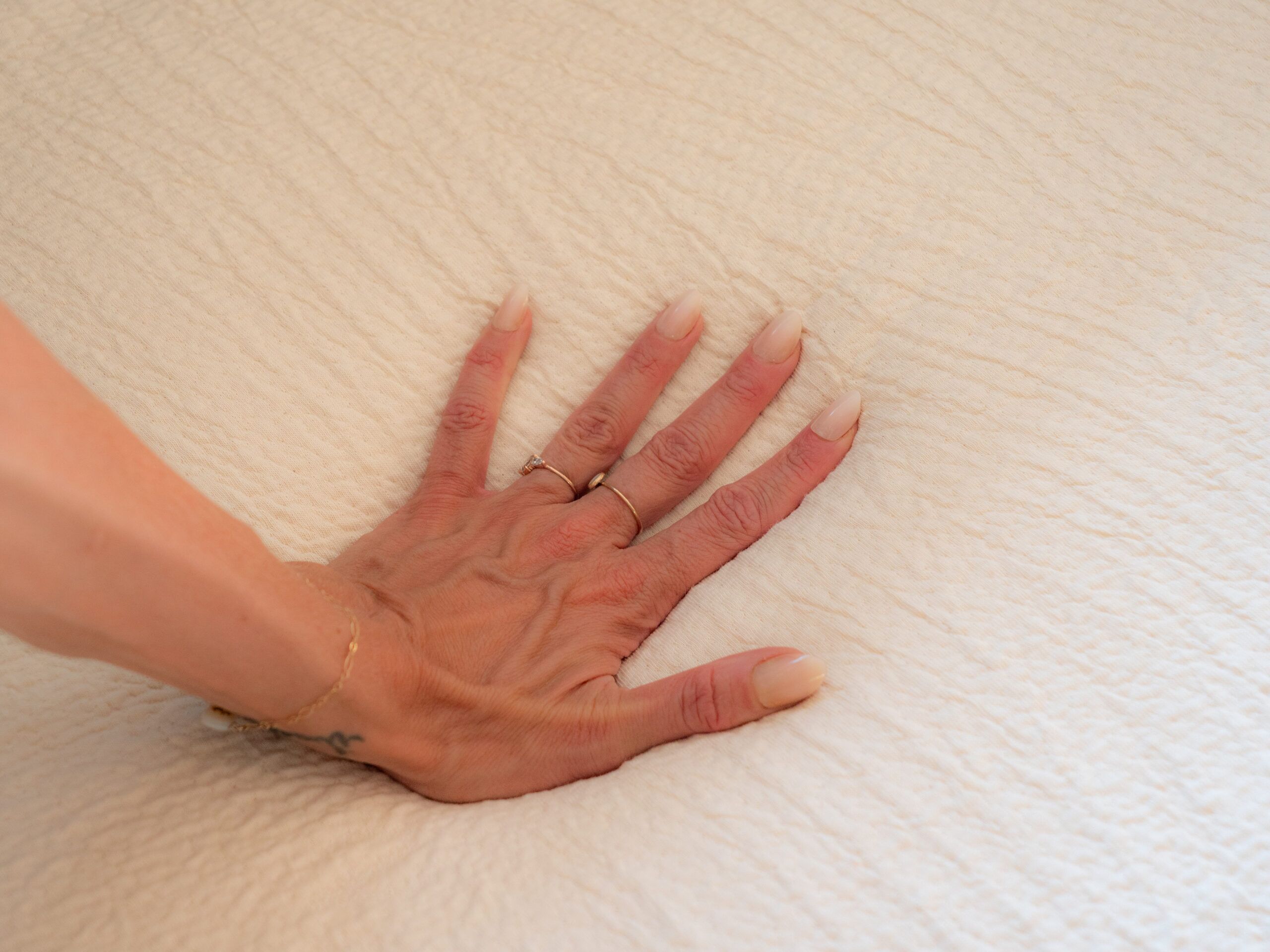 A hand with manicured nails presses down on a textured, light-colored fabric surface, causing a visible indentation.