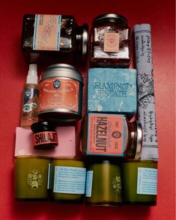 Various jars, candles, soaps, and a rolled cloth with labels are arranged neatly on a red background.