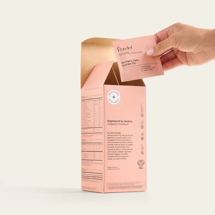 A hand removes a pink daily vitamin packet from an open Perelel supplement box.