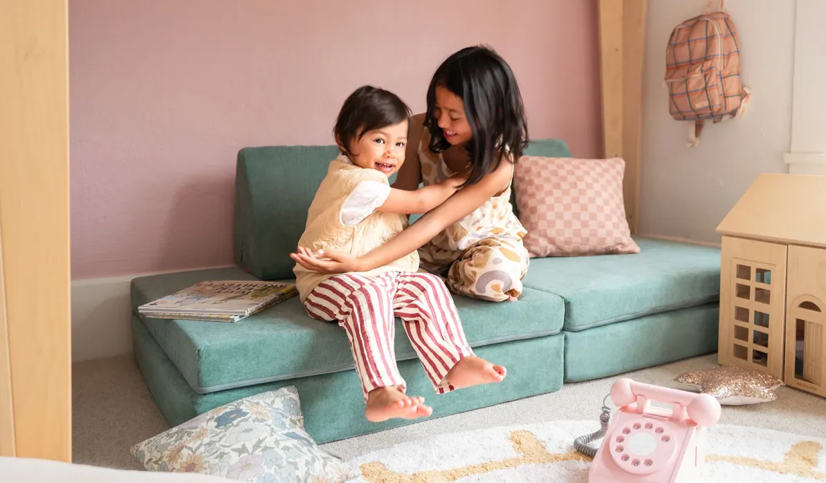 Two children sitting together and playing on a teal modular foam sofa.