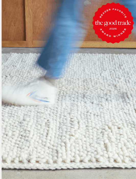 A person in blue jeans and white shoes walks on a textured, off-white rug; a red "The Good Trade 2026 Award Winner" badge appears in the top right corner.