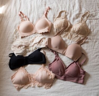 Six various bras in nude, black, and mauve lace and smooth styles laid out on a white fabric surface.