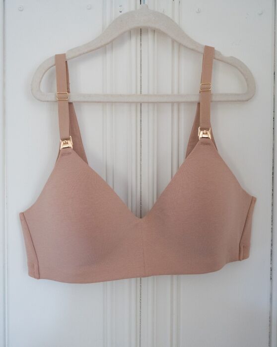 Nude-colored nursing bra with gold-toned clips on the straps, hanging on a hanger.