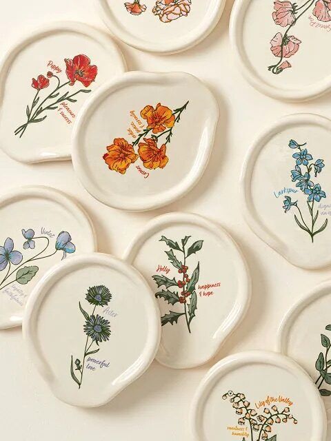 Several irregularly shaped ceramic plates with botanical illustrations and names of different flowers are arranged on a light surface, perfect for adding charm to your online shopping finds.