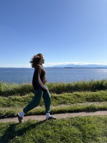 A person walks along a grassy path beside a large body of water under a clear blue sky.