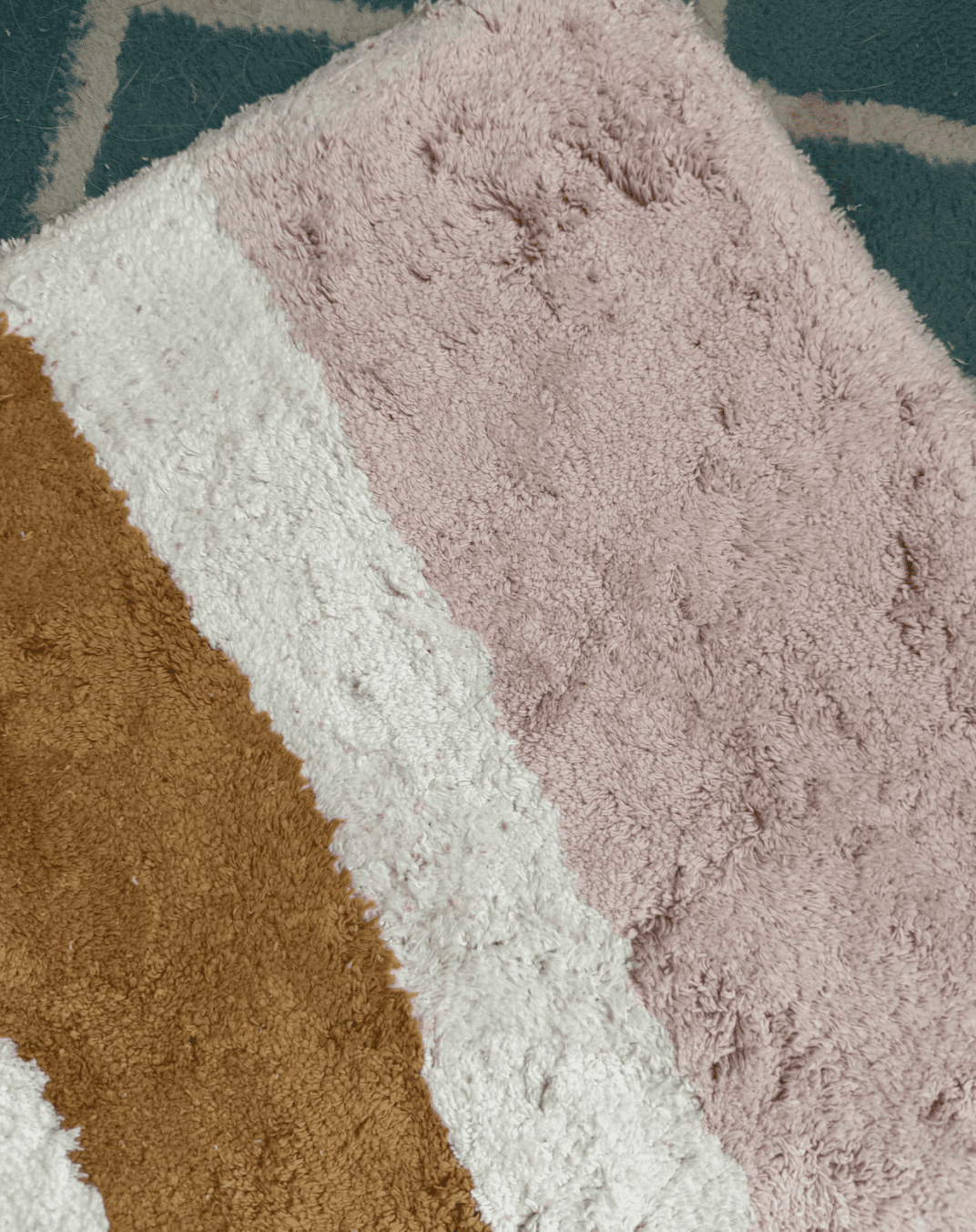 A close-up of a textured rug with diagonal stripes in pink, white, and brown on top of a blue and white patterned carpet.