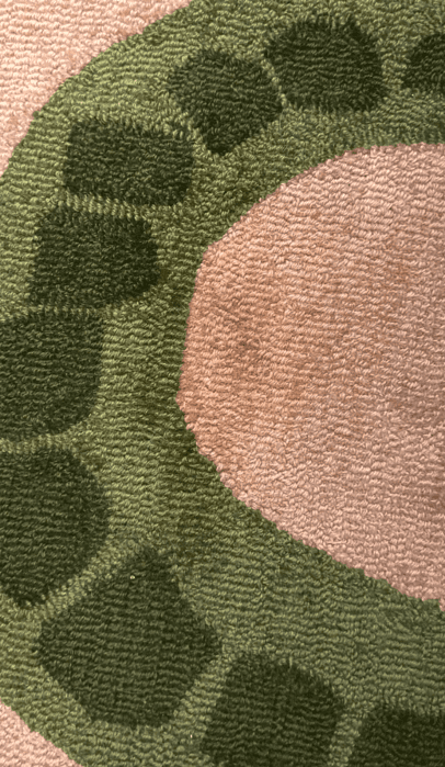 Close-up of a textured carpet with a large green curved pattern bordered by smaller green shapes on a pink background.