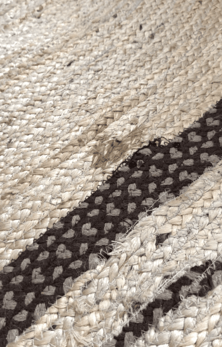 A close-up of a woven rug with tan and brown patterns, showing a frayed and damaged spot near one of the darker stripes.