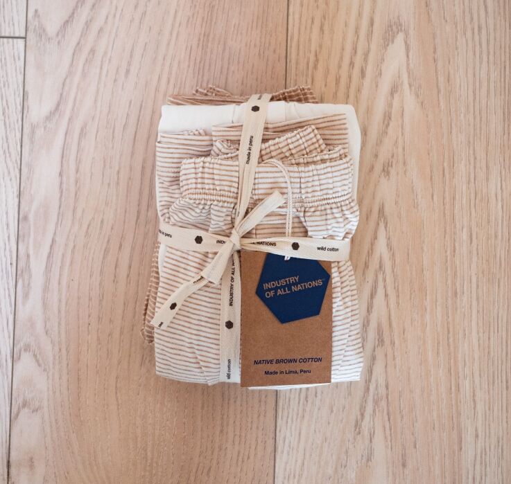 A set of folded, beige-striped cotton garments tied with a printed ribbon and tag, placed on a wooden surface.