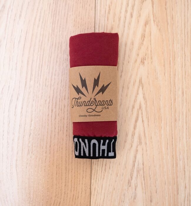 A pair of red Thunderpants underwear rolled up with a brown branded paper band, placed on a light wooden surface.