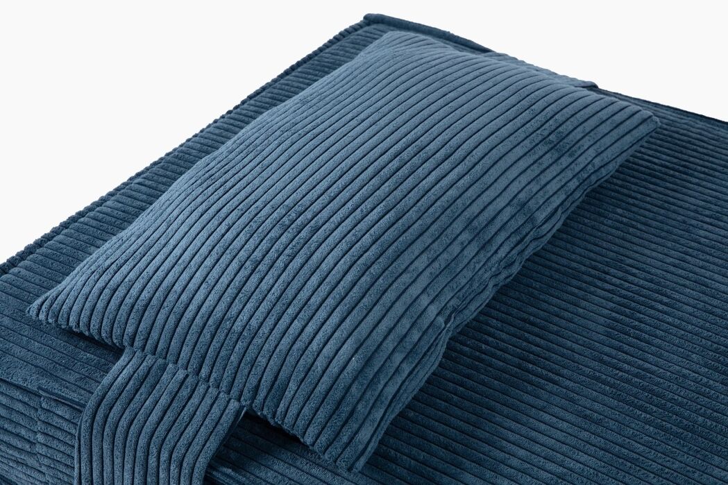 A blue corduroy pillow rests on a matching corduroy blanket, both featuring a ribbed texture and clean, modern lines.