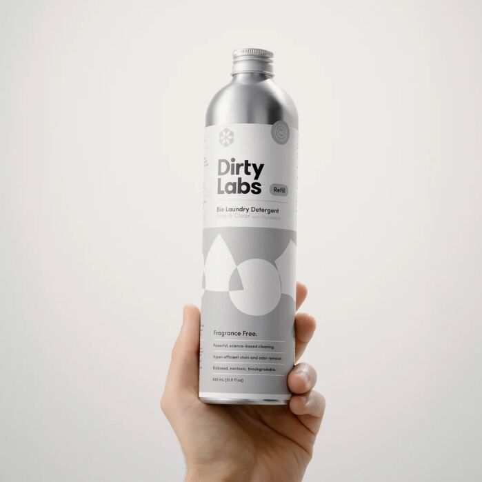 Hand holding a silver bottle labeled “Dirty Labs Bio Laundry Detergent,” fragrance free, with minimalist design against a plain white background.