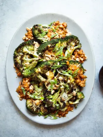 Roasted broccoli steaks topped with chopped peanuts and sliced scallions, served over a bed of saucy chickpeas on an oval white plate.