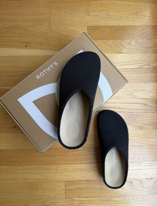 A pair of black Rothy’s slip-on shoes resting on top of a Rothy’s branded cardboard box.