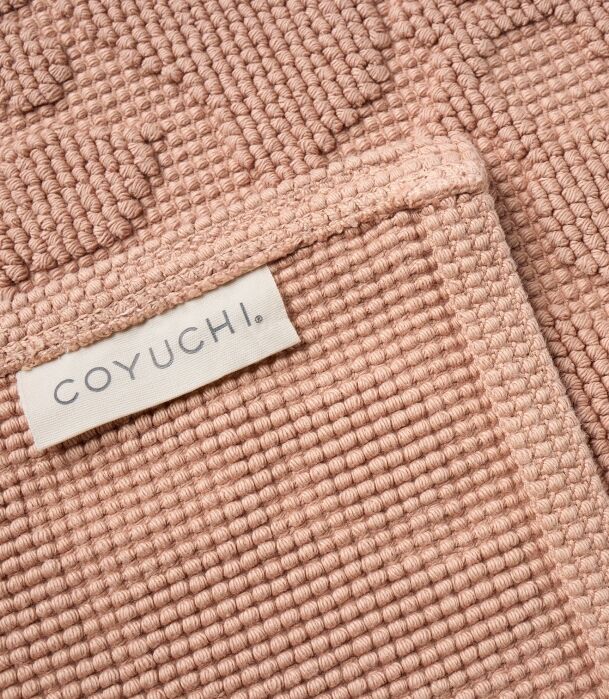 Close-up of a textured pink mat or towel with a COYUCHI brand label sewn on one corner.