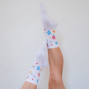 Two legs raised against a white wall, wearing organic socks with colorful floral patterns.