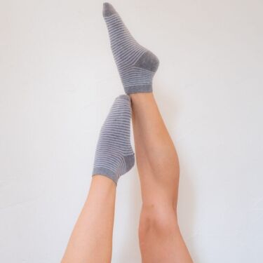 Two legs raised against a white background, one foot wearing a gray striped organic sock and the other bare.