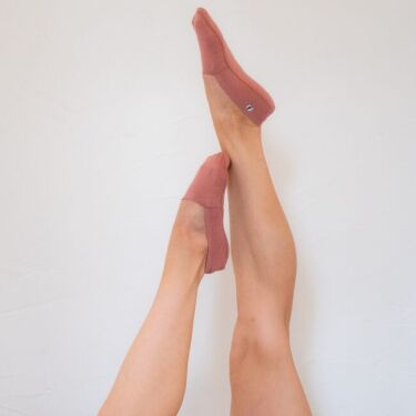 Two legs extended upward against a white wall, each foot wearing pink organic socks.