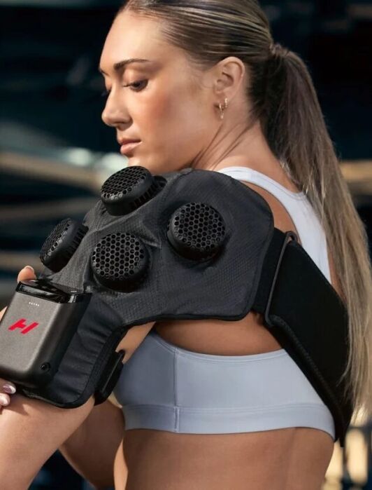 A person wearing a black wearable massage device on their shoulder.