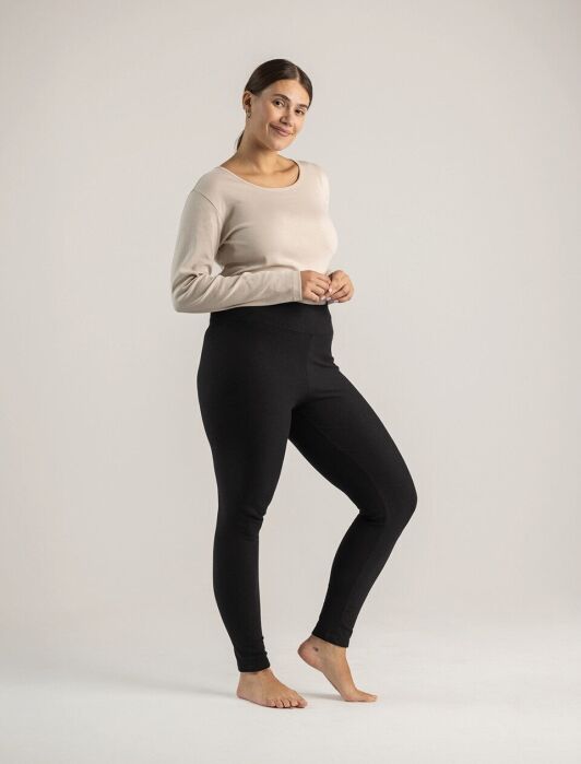 A woman wearing a beige long-sleeve top and black high-waisted leggings.