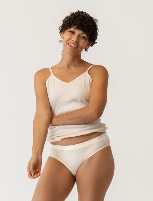 A smiling person wearing a cream-colored camisole and matching briefs.