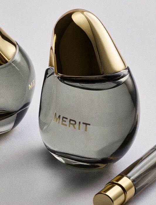 Two teardrop-shaped perfume bottles with gold caps and a matching pen-shaped applicator, all labeled “MERIT.”