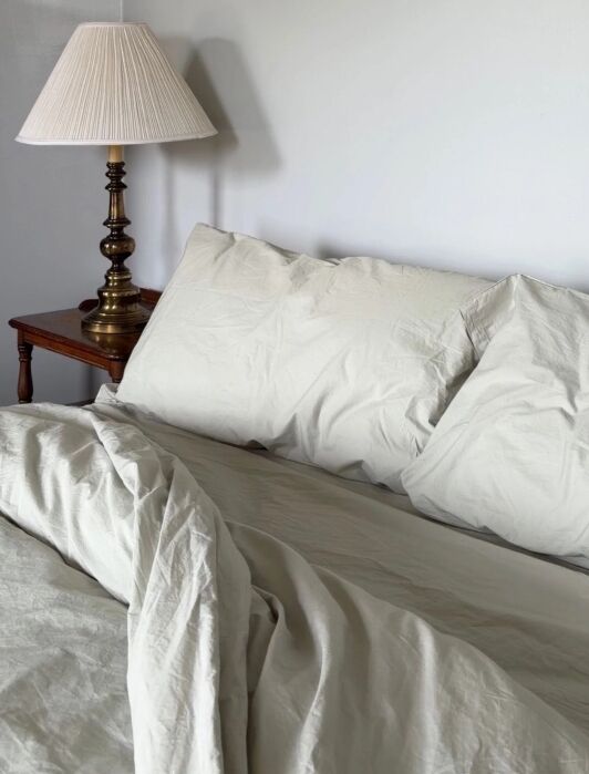 A bed with light-colored bedding next to a nightstand with a brass lamp.