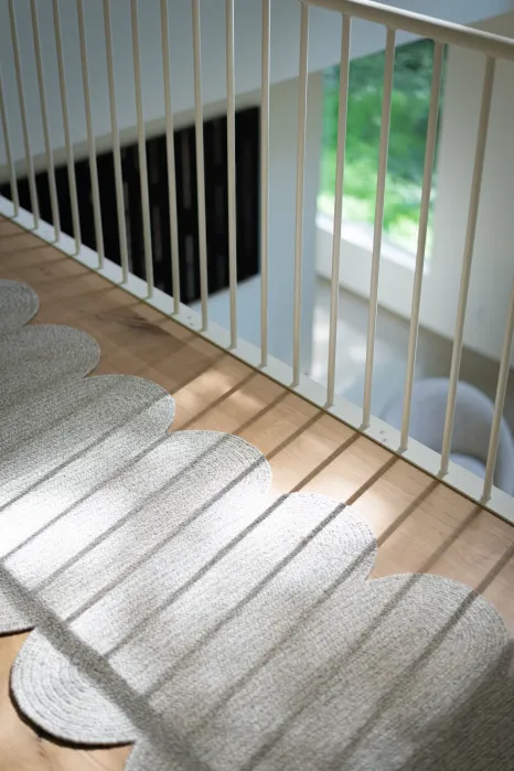 A scalloped-edge runner rug on a hardwood floor next to a white metal stair railing.