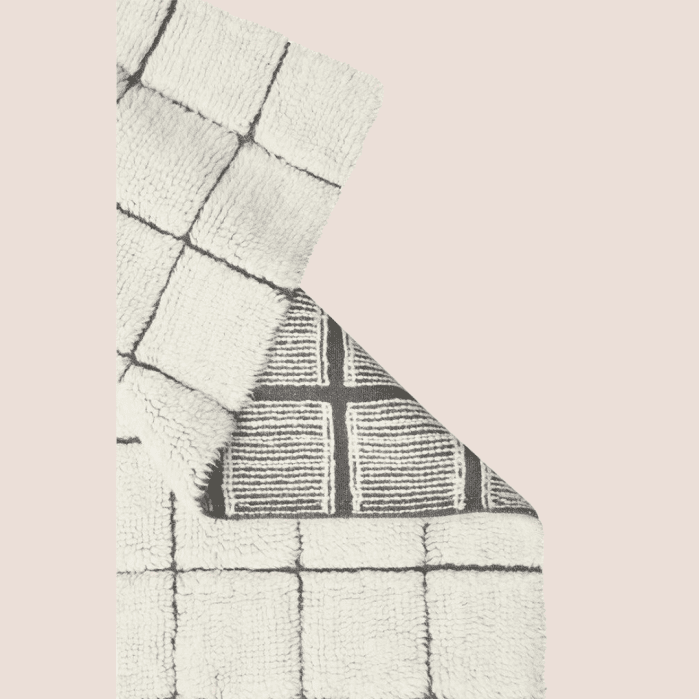 A folded rug featuring a white base with a black grid pattern, showing the patterned underside.