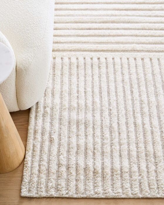 Cream-colored area rug with a textured vertical striped pattern next to a curved armchair.
