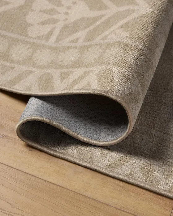Beige rug with a patterned surface folded over to show its underside on a wooden floor.
