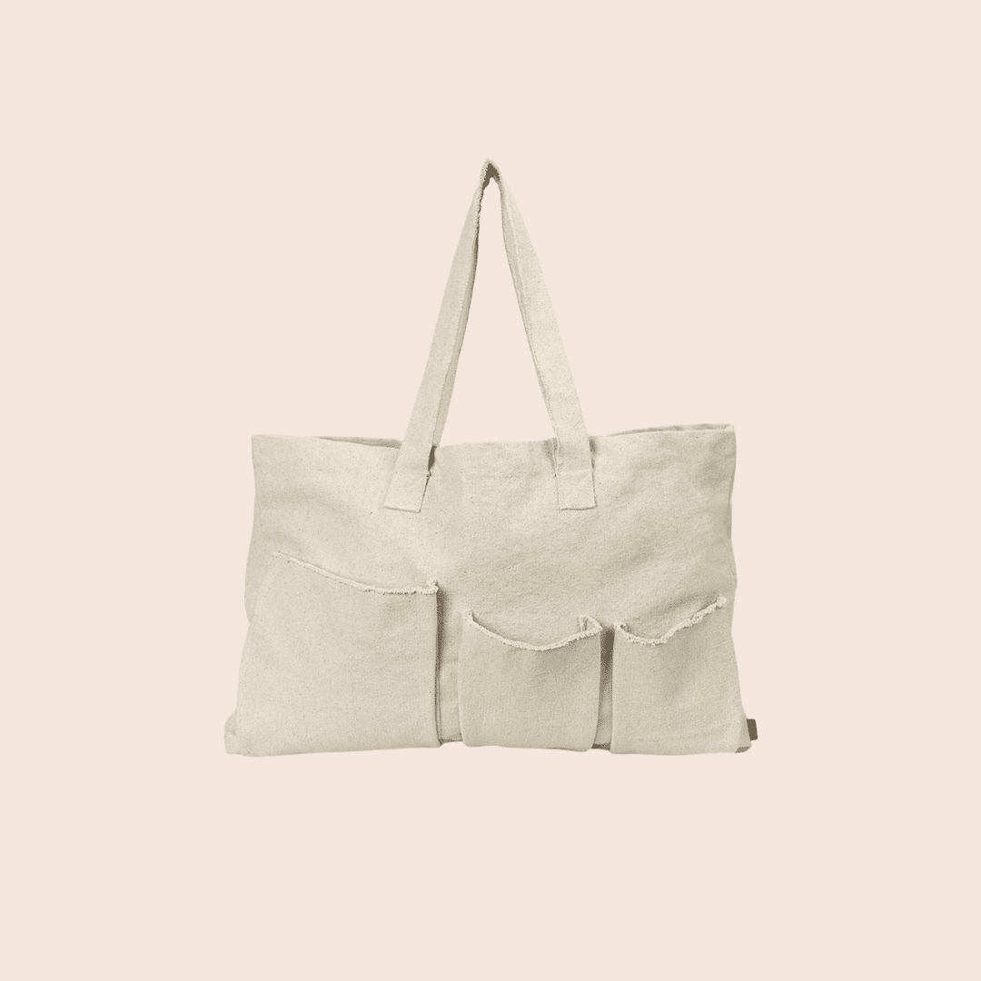 Off-white canvas tote bag with two shoulder straps and three exterior pockets with raw-edged trim.