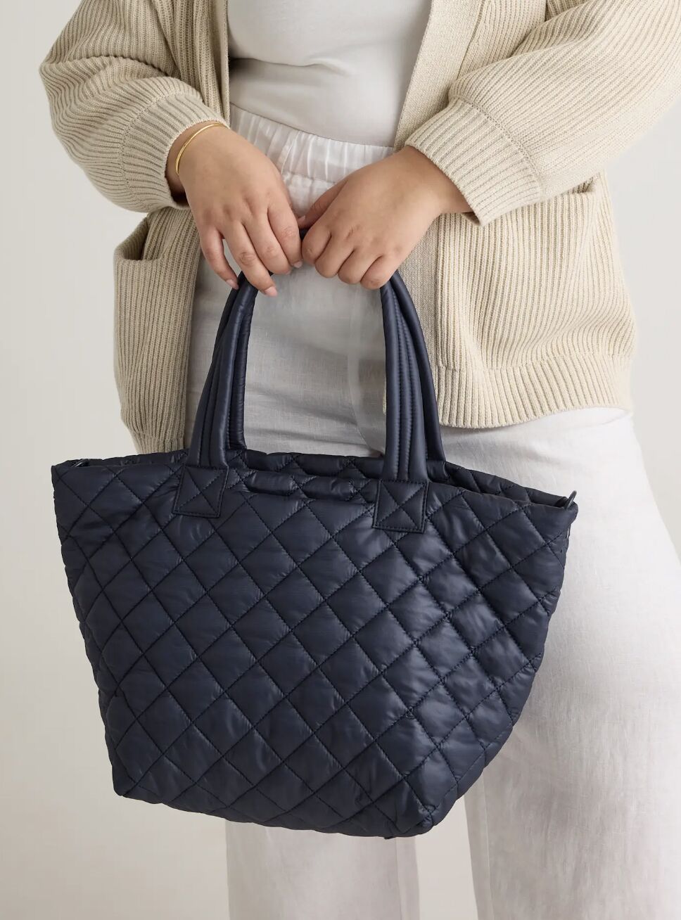 A person holding a dark blue quilted tote bag.