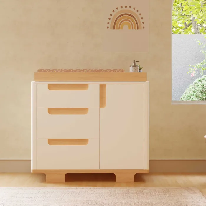A nursery changing table with three drawers and a side cabinet, topped with a changing pad and a small dispenser.