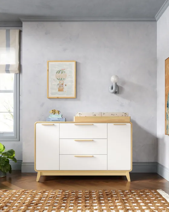 White wooden nursery dresser with a changing tray on top, featuring a framed hot air balloon illustration and a small elephant figurine.