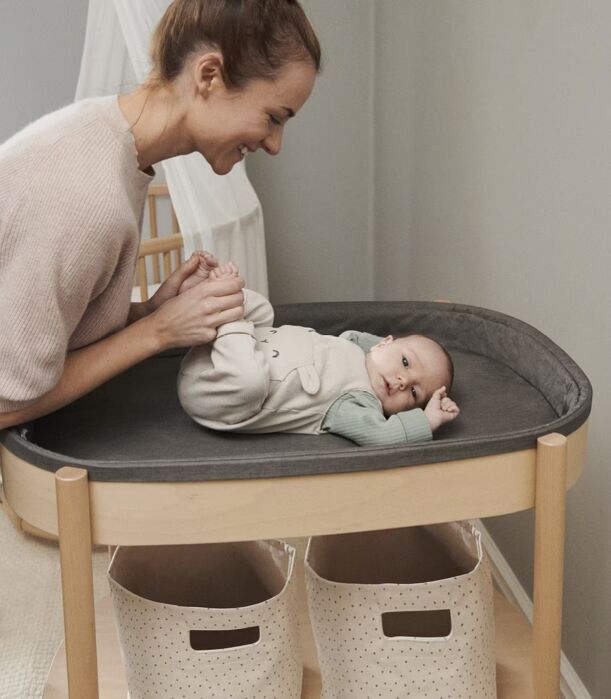 A woman smiling while holding the feet of a baby lying on a changing table.